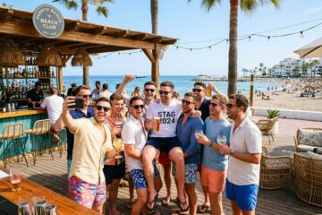 A group of young men enjoying a sunny day together near the beach with the sea and palm trees in the background.